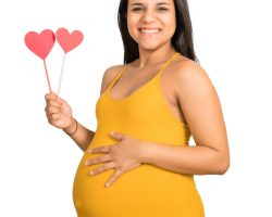 Close-up of pregnant woman holding heart sign against white background. Pregnancy, motherhood concept.